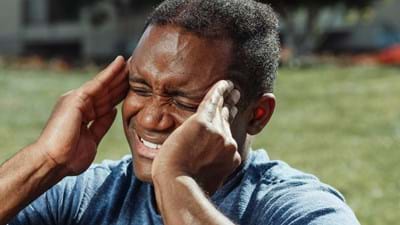 Man outdoors holding his head, appearing in pain—may benefit from acupuncture or tcm.