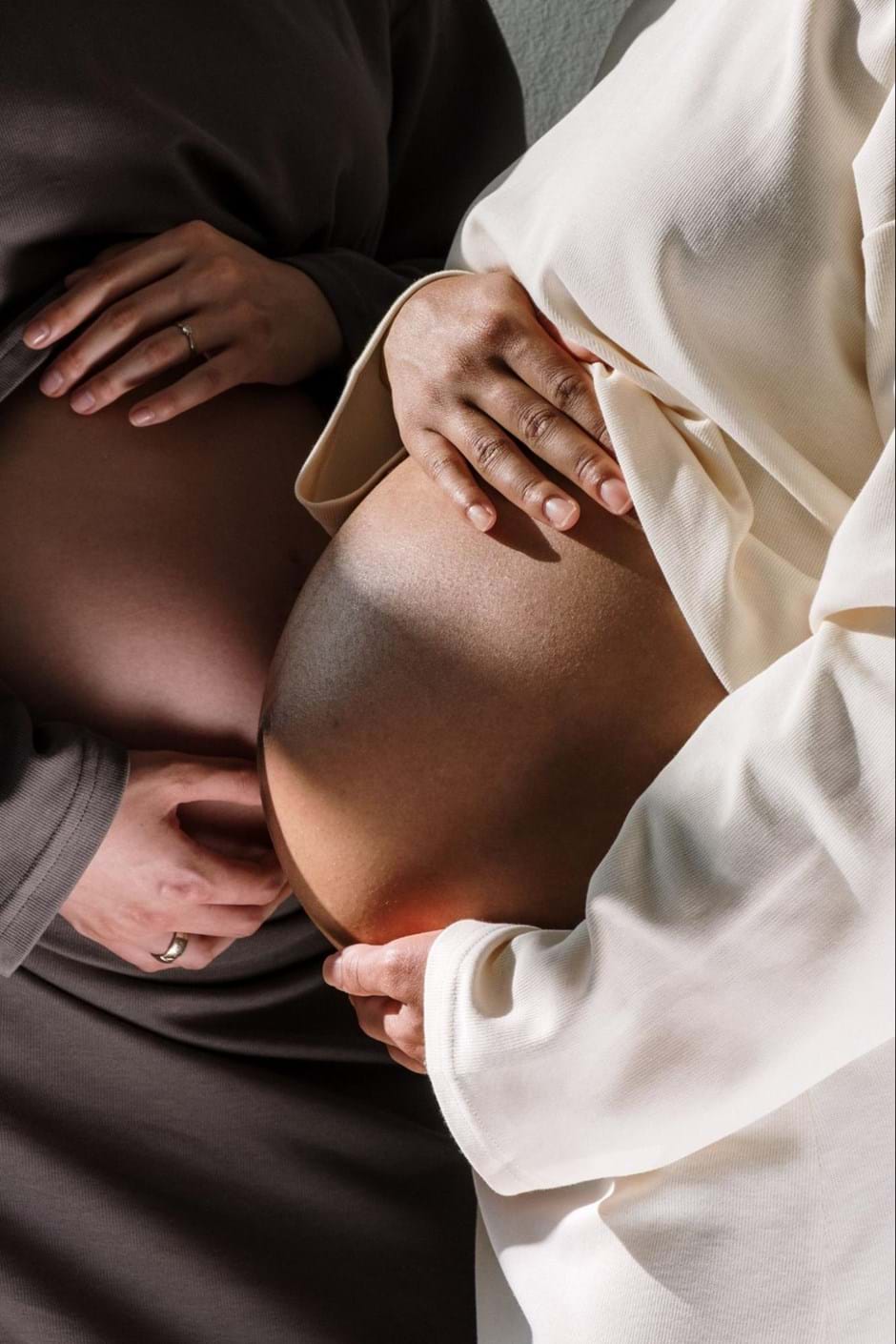 Two pregnant people touch bare bellies side by side, sharing their TCM and wellness journey.