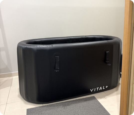 A black inflatable tub labeled "VITAL+" evokes TCM on a tiled floor beside a gray mat.