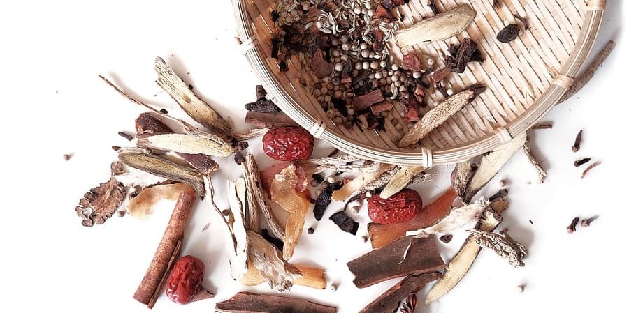 A basket with assorted dried herbs and spices, used in Chinese herbal medicine, spills out.