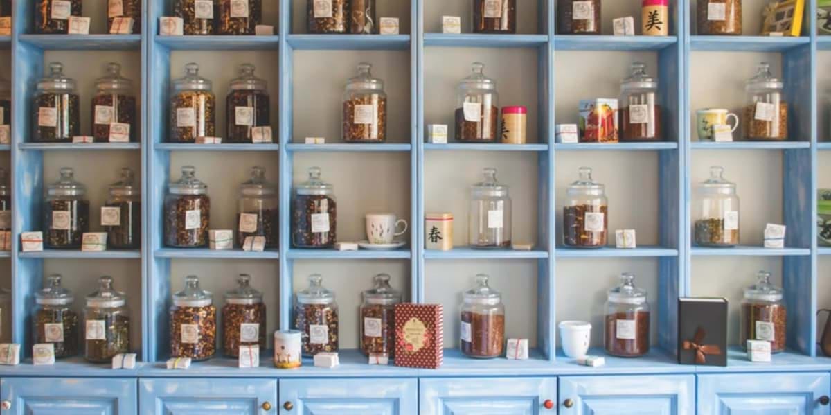 Glass jars with herbs and teas, highlighting Chinese herbal medicine, on blue shelves in a shop.