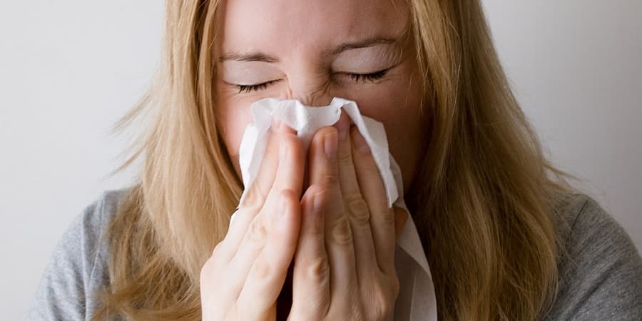 Woman sneezing into a tissue, seeking relief through acupuncture or chinese herbal medicine.