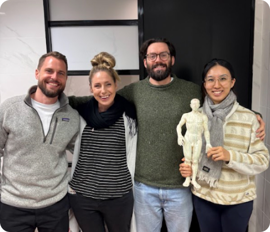 Four people standing together indoors, one holding a human anatomy model.