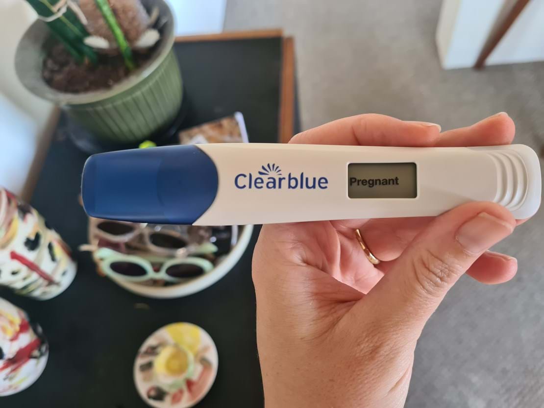 A hand holds a Clearblue pregnancy test showing a positive result after using TCM.