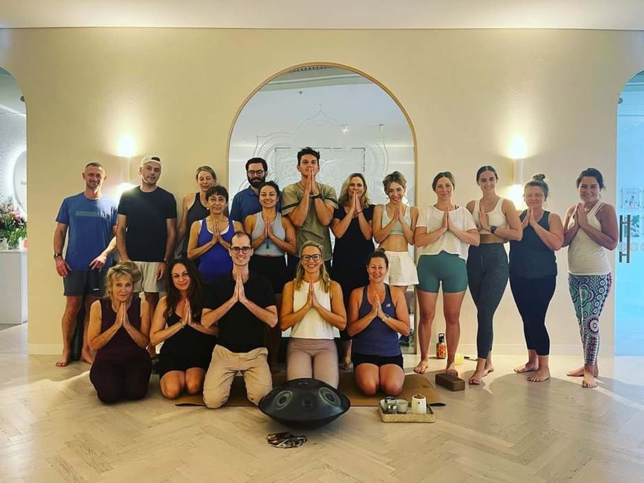 Group of people in yoga attire, smiling in prayer pose—embracing yoga and TCM wellness.