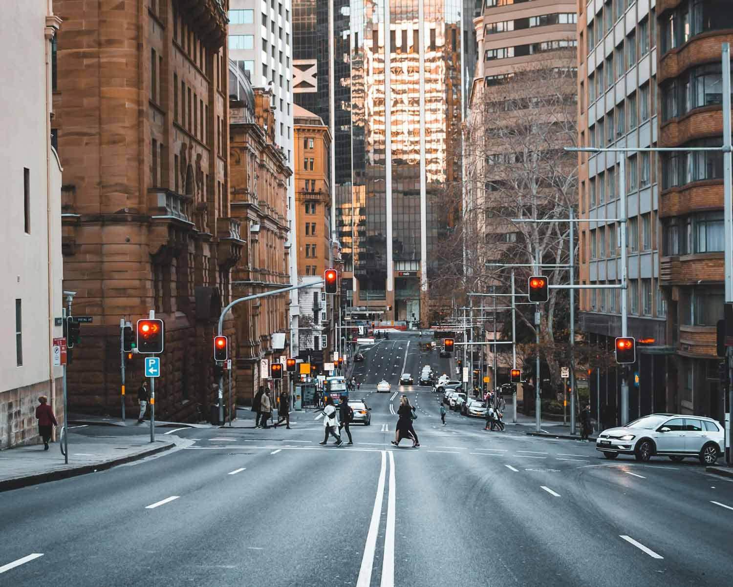 People crossing a city street at a crosswalk, near buildings and a TCM clinic in view.
