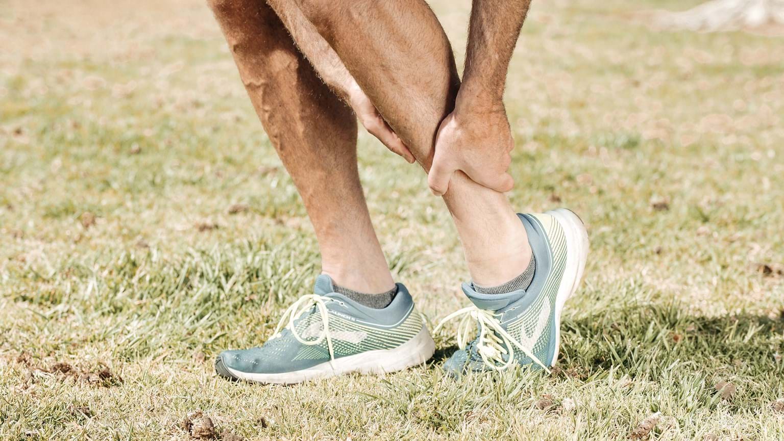 Person in running shoes on grass holding sore leg, possibly seeking relief with acupuncture.