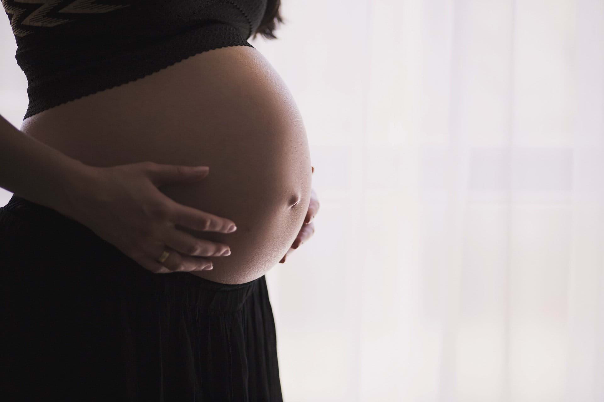 Person holding their pregnant belly, standing by a window after a tcm acupuncture session.