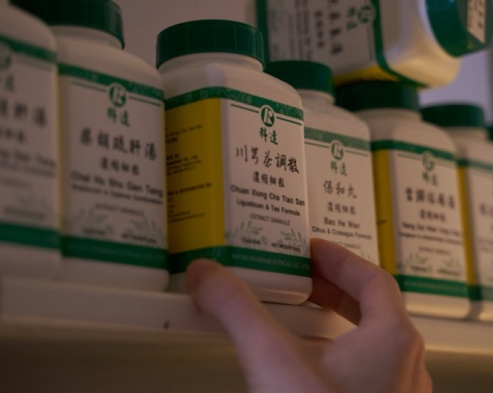 A hand reaches for a white bottle of herbal supplements labeled in Chinese on a shelf.