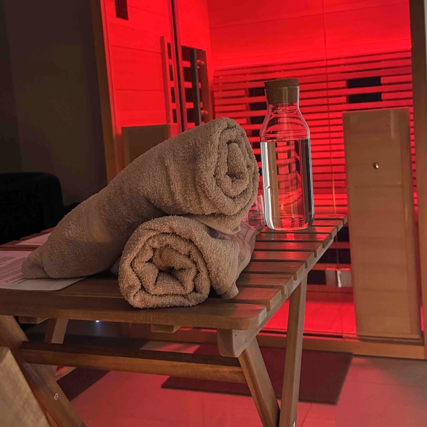 Two rolled towels and a glass water bottle on a table in a TCM-inspired, red-lit room.
