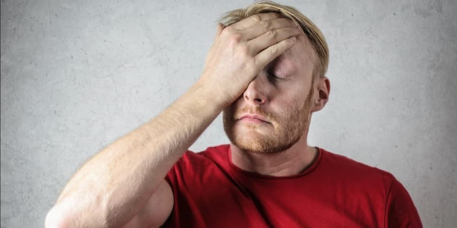 Man in a red shirt appears frustrated, considering tcm or acupuncture for relief.