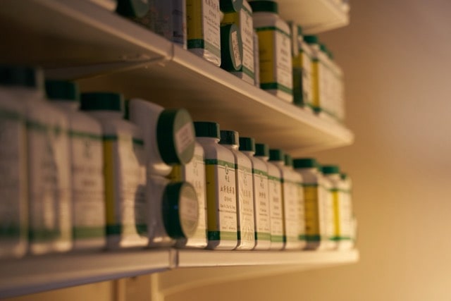 Rows of plastic bottles with green caps are arranged on white shelves.