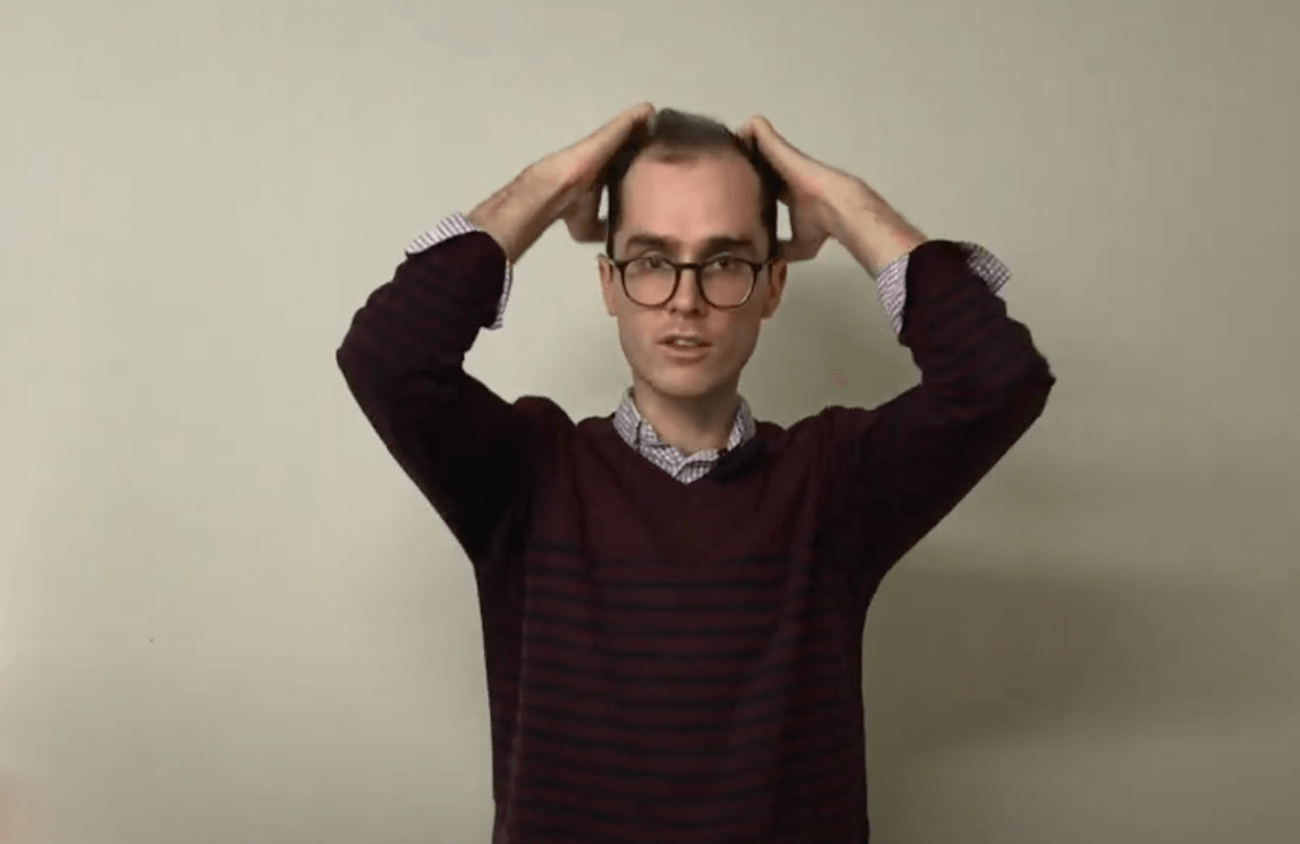 Person wearing glasses holding both hands on head, evoking TCM or acupuncture relaxation techniques.