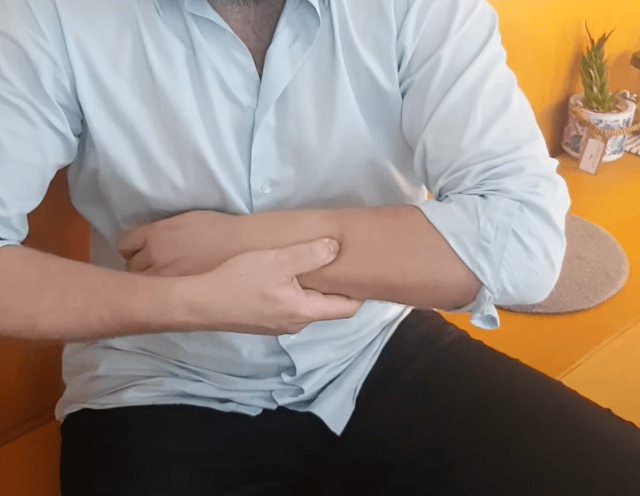 Person sitting on a couch holding their forearm, considering acupuncture for relief.