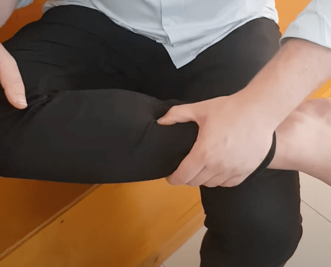 Person holding their knee, possibly seeking relief through acupuncture, on a wooden bench.