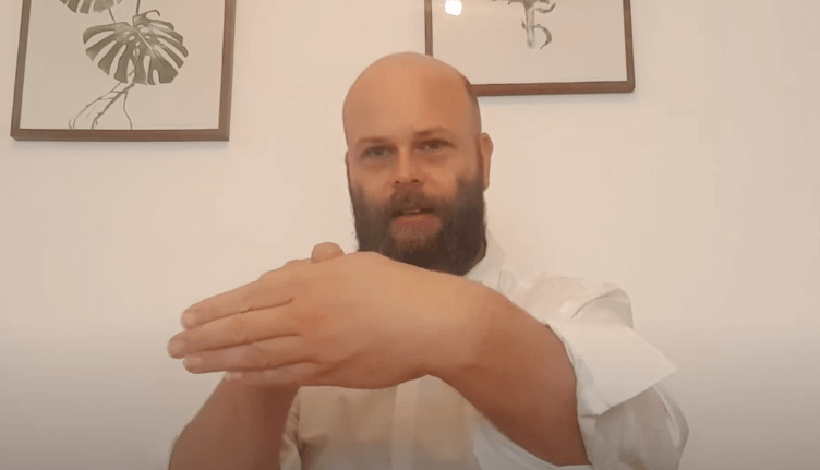 A man in a white shirt discusses TCM, gesturing as he sits before framed art.