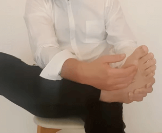 Person in a white shirt sits, holding their bare foot as in a TCM or acupuncture session.