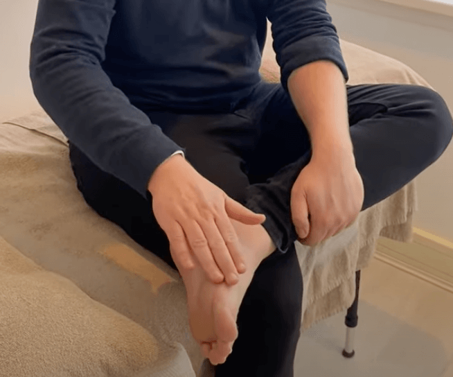 A person is sitting cross-legged, touching their foot as in an acupuncture session.