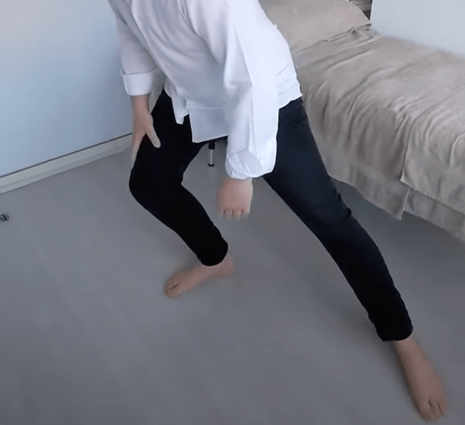 Person in a white shirt and black pants doing a wide-leg stretch, inspired by TCM practices.