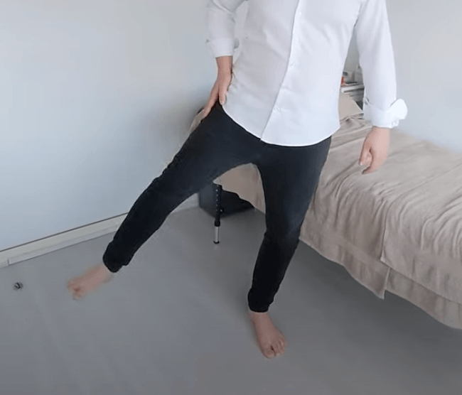 Person in a white shirt and black pants practices tcm balance on one leg in a bedroom.
