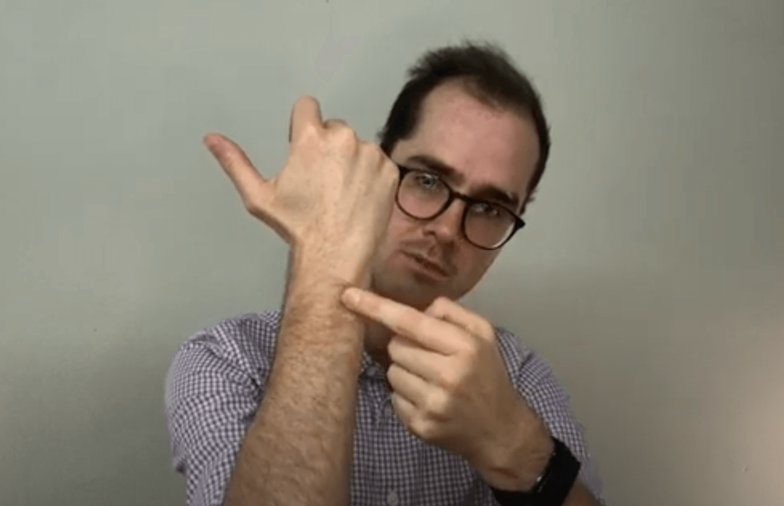 Man in glasses points to his wrist, demonstrating a TCM acupuncture point with his other hand.