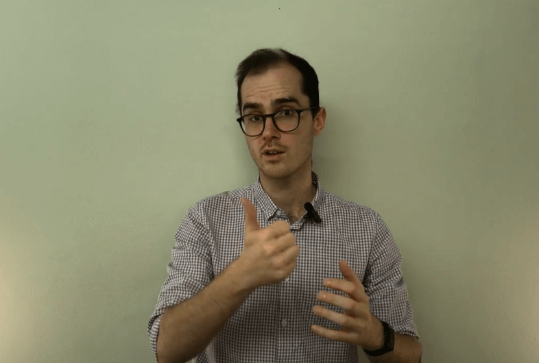 Man in glasses gestures with left hand, wearing checkered shirt, suggesting TCM expertise.