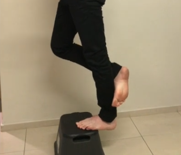 Person practicing balance on a black step stool, inspired by TCM principles indoors.