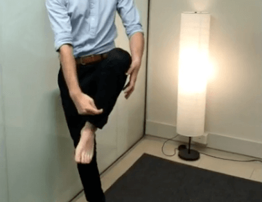 Person in business attire balancing on one foot, showcasing TCM-inspired balance indoors.