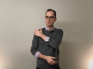 Man touching his left shoulder, possibly seeking relief with acupuncture or tcm, against a plain wall.