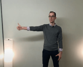 Person standing indoors, arm extended sideways with thumb up, near a TCM floor lamp.