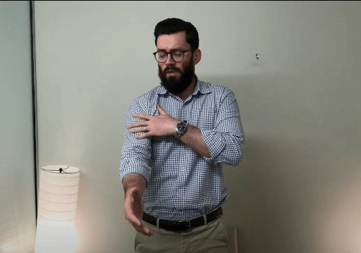 Man in glasses touches his left shoulder, possibly considering acupuncture, beside a lamp.