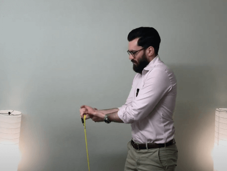 Man measures with a tape measure, standing by two floor lamps in a TCM clinic setting.