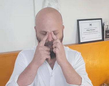 A man in a white shirt practices TCM, pressing his fingers to the bridge of his nose, eyes closed.