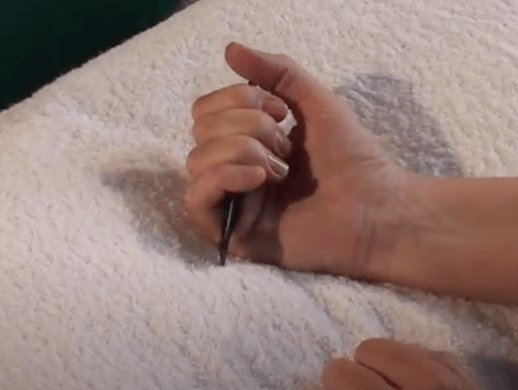 A hand grips a pen in a fist over a white surface, hinting at tcm practice.