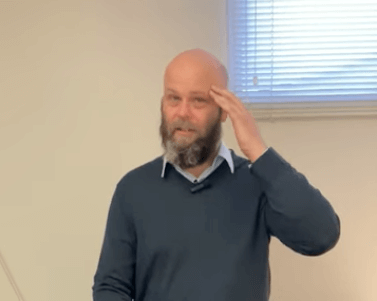 A bearded man in a dark sweater reflects by a window, considering acupuncture indoors.