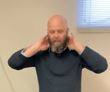 A man with a beard touches his neck, possibly seeking relief through acupuncture indoors.