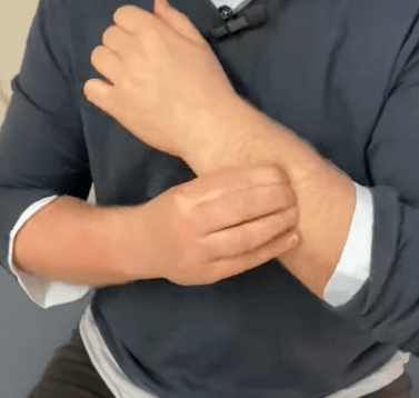 Person scratching their left forearm, considering tcm remedies, while seated.