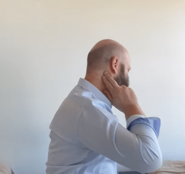 Man sitting, touching his neck, possibly seeking relief through acupuncture or TCM.