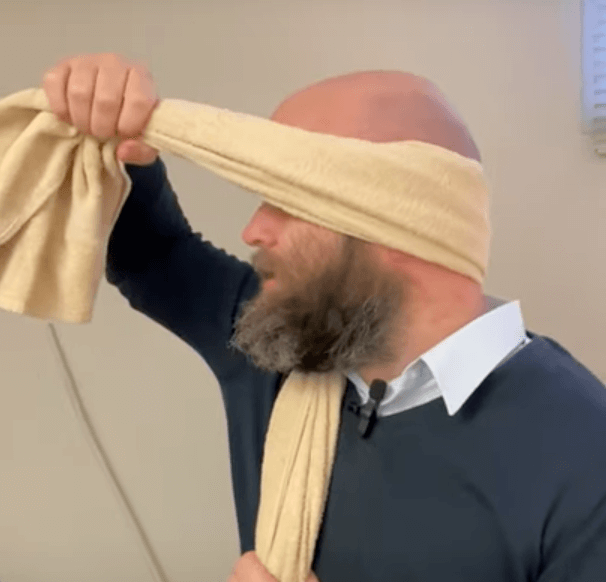 A man wraps a beige towel around his head after an acupuncture or TCM session.