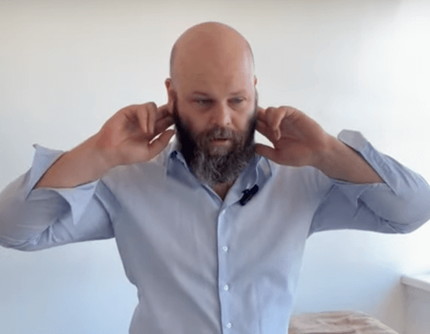 A man with a beard blocks his ears indoors, seeking relief through TCM or acupuncture.