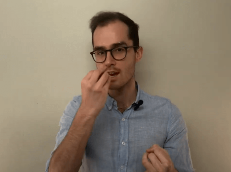 A man in glasses gestures near his mouth, illustrating a tcm technique against a plain background.