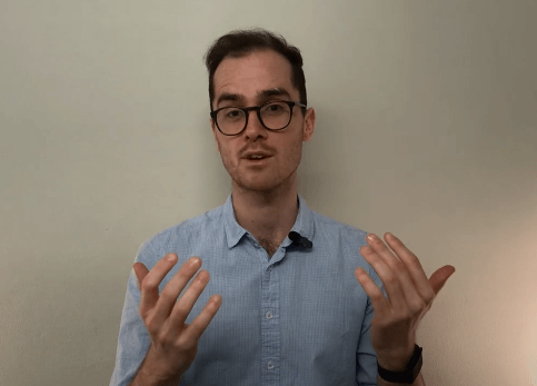 A person in glasses gestures while discussing acupuncture against a plain background.