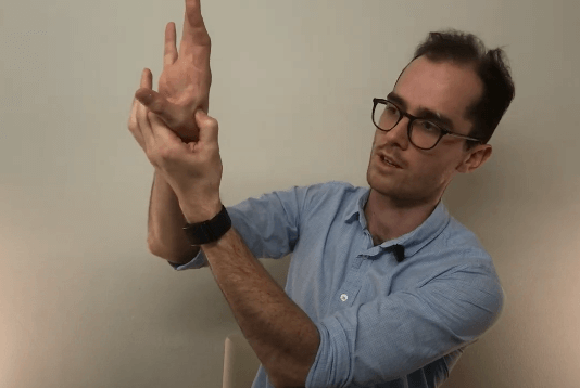 A man in glasses practices TCM stretches using his right hand against a plain background.
