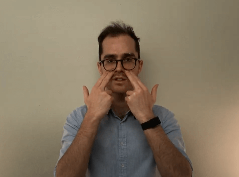 Man pointing to both sides of his nose, referencing acupuncture points while facing the camera.