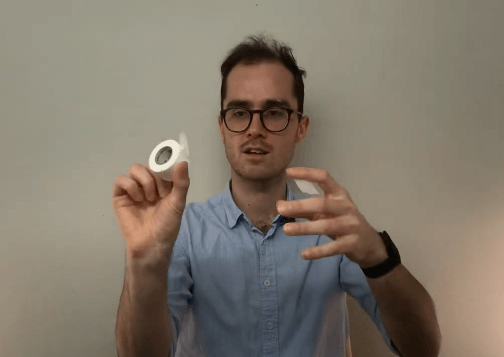 Person in glasses holding tape, gesturing as if explaining TCM or acupuncture techniques.