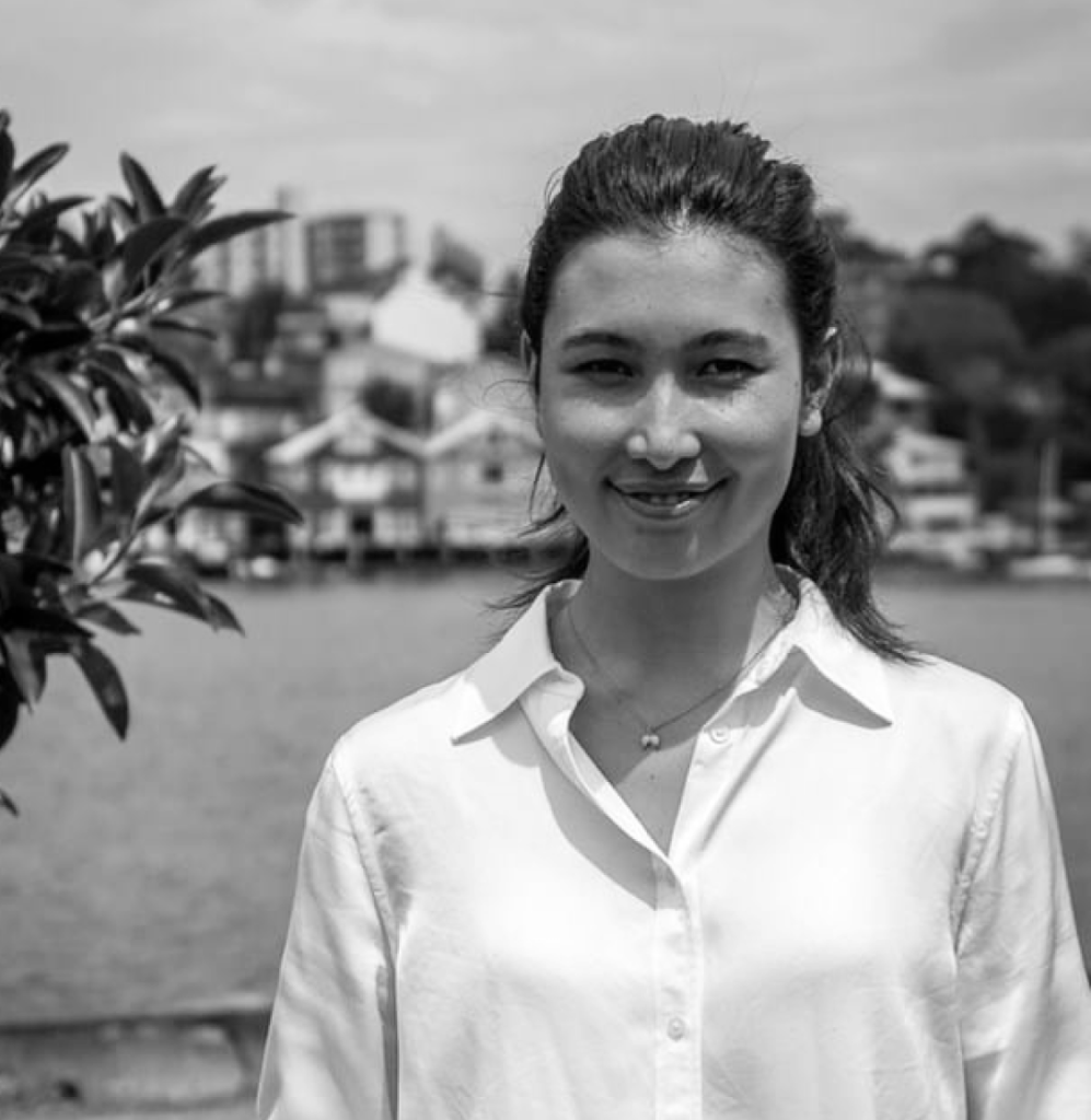 Woman in a white shirt outdoors, with water, buildings, and a touch of TCM tranquility.