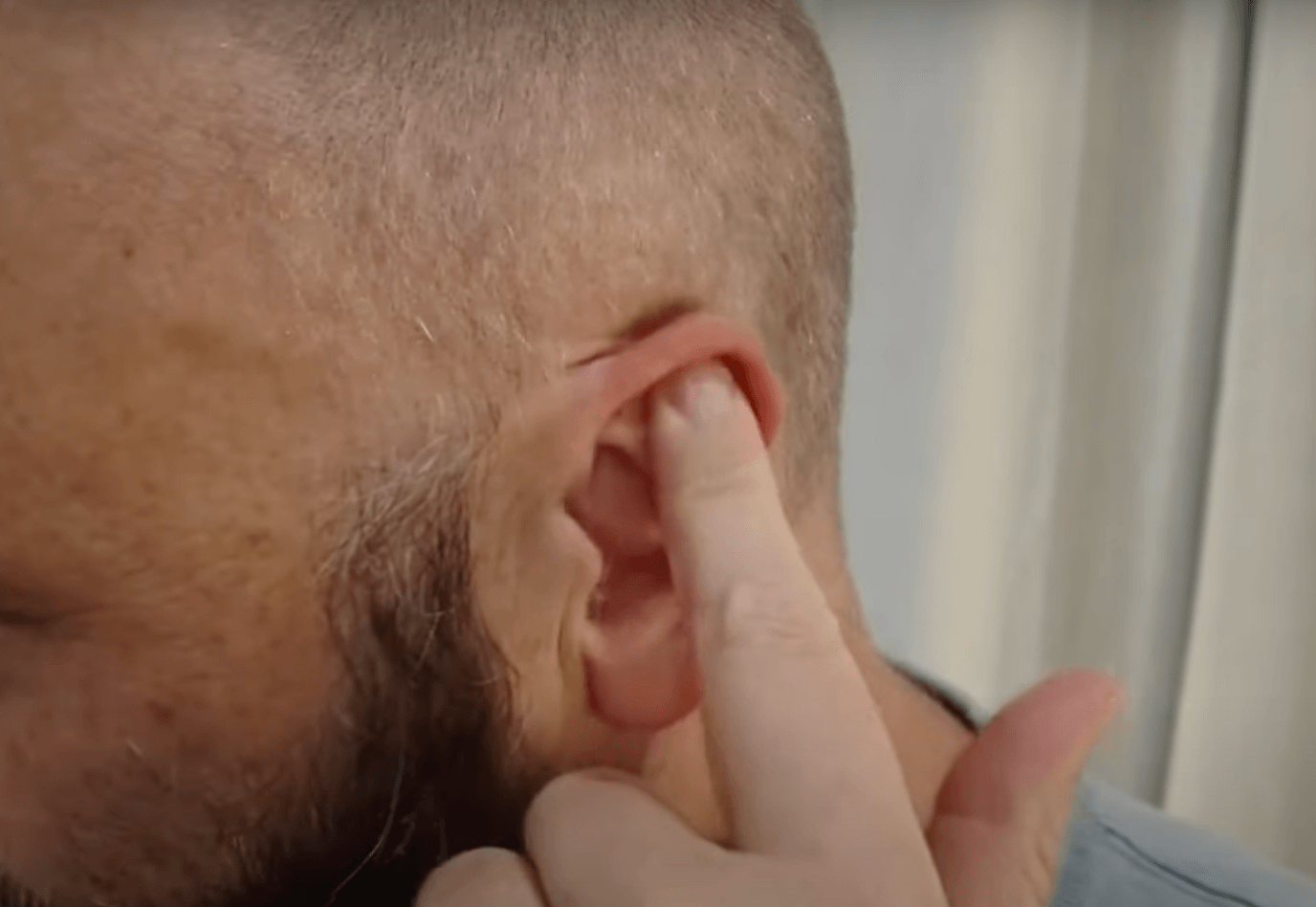 A person points a finger to the top part of their ear, indicating an acupuncture point.